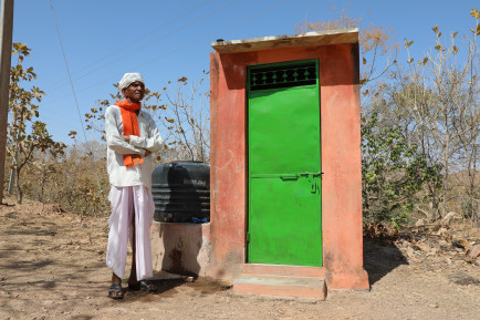 Man stood next to an outdoor toilet